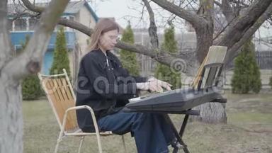 专业可爱的女钢琴家在后院的合成器上演奏古典钢琴音乐。 真人系列。